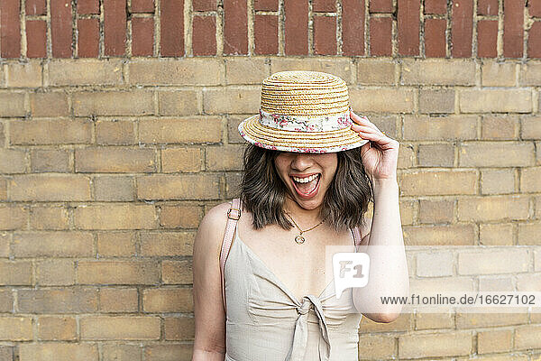 Glückliche Frau mit Hut an einer Mauer stehend