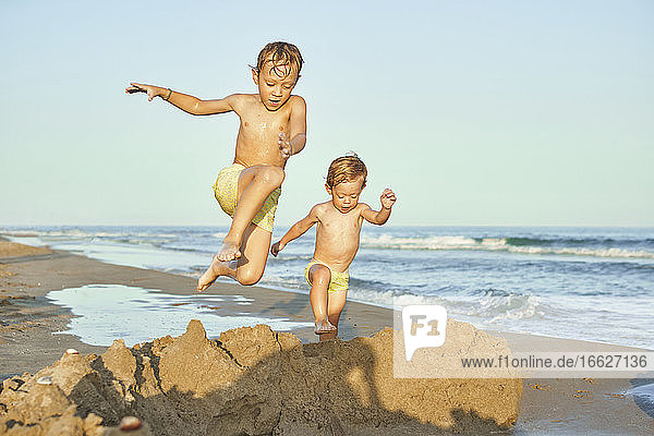 Boys jumping on sand while playing at beach