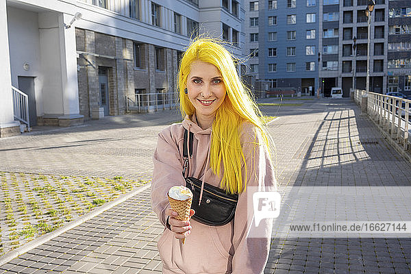 Woman holding ice cream cone while standing on street during sunny day