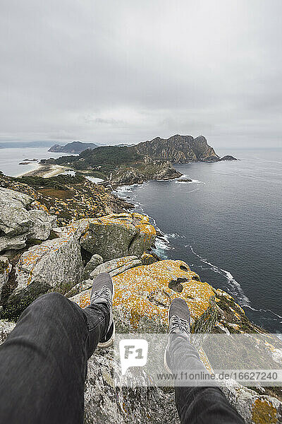 Low section of young male tourist over rock formation against cloudy sky  Cíes Islands  Vigo  Pontevedra Province  Galicia  Spain