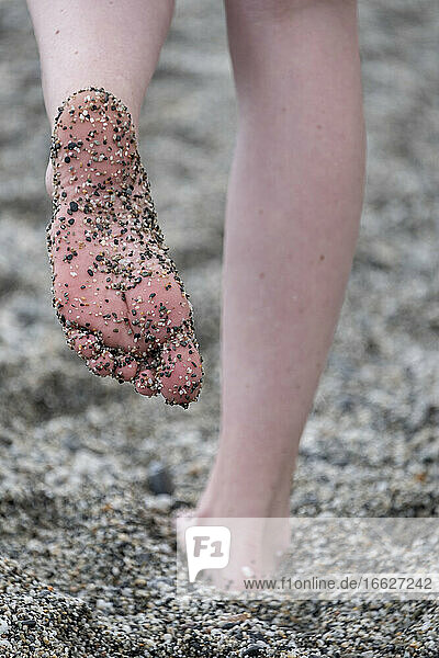 Frau  die am Strand steht und deren Fuß mit Kies bedeckt ist