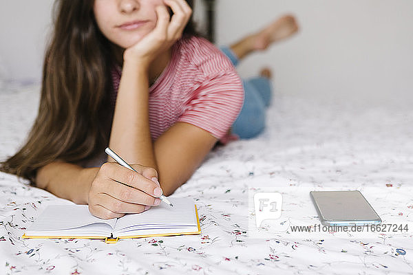 Woman taking notes in book while lying down on bed at home