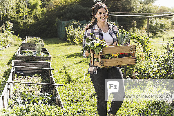 Junge Frau trägt Kiste mit Gemüse beim Spaziergang im Gemeinschaftsgarten