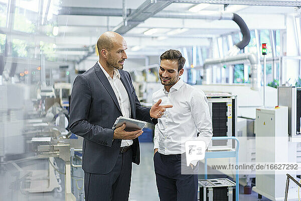 Confident businessman discussing with engineer over digital tablet at factory