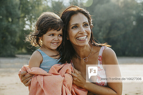 Lächelnde Mutter legt Handtuch um ihre Tochter am Strand