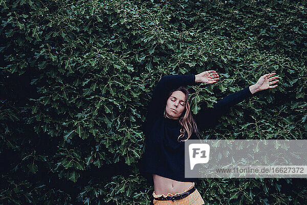 Woman with hand raised standing against leaves wall