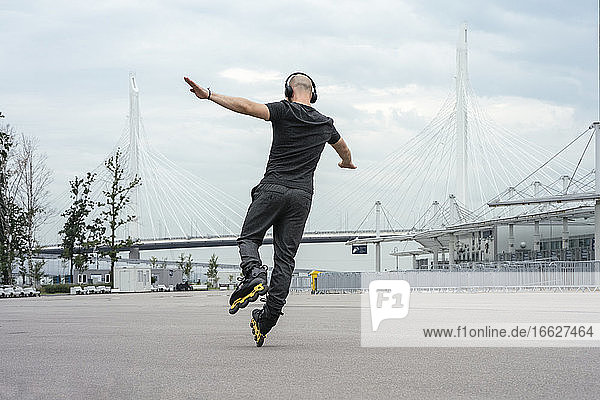 Young man with arms outstretched listening music while inline skating on road