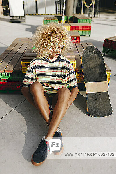 Afro blonde Frau sitzt am Skateboard an einem sonnigen Tag