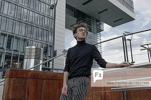 Nachdenklicher junger Mann  der wegschaut  während er am Geländer eines Gebäudes in der Stadt steht