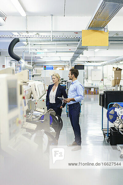 Young engineer discussing with mature businesswoman while standing by machinery at factory