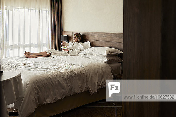 Retired woman eating fresh fruits while relaxing on bed at hotel room during vacation
