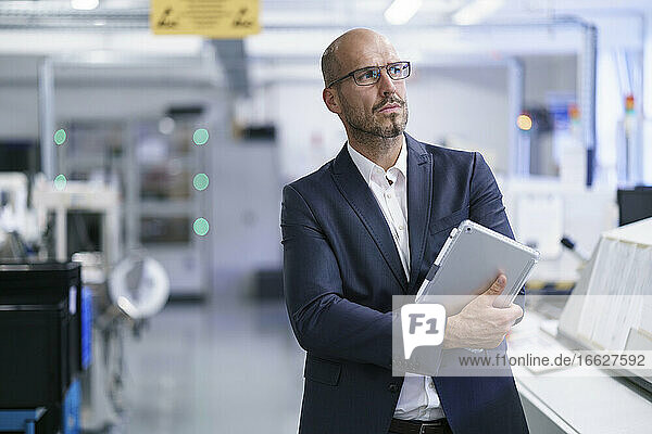 Geschäftsmann  der ein digitales Tablet hält  während er in eine helle Fabrik blickt
