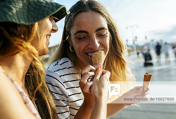 Lächelnde junge Frau  die ihre Schwester mit Eiscreme füttert  während sie sich in der Stadt vergnügt