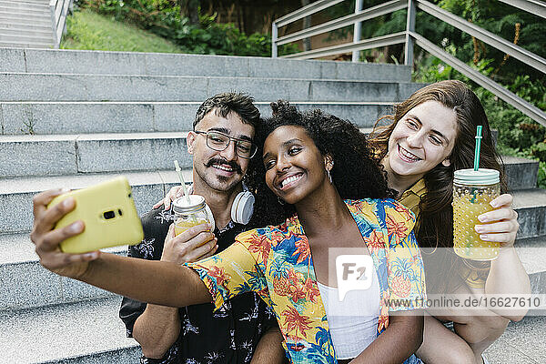 Freunde machen ein Selfie mit ihrem Smartphone  während sie in einem öffentlichen Park sitzen