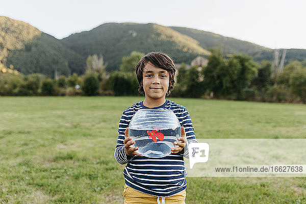 Lächelnder Junge hält ein Fischglas in der Hand  während er im Hinterhof steht