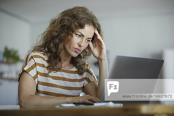 Frau sitzt mit dem Kopf in den Händen und arbeitet zu Hause am Laptop