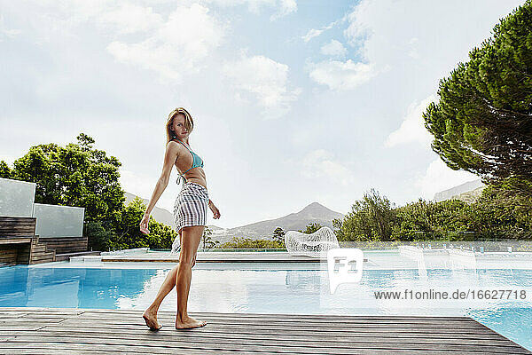 Junge Frau im Bikini steht in der Nähe des Pools an einem sonnigen Tag