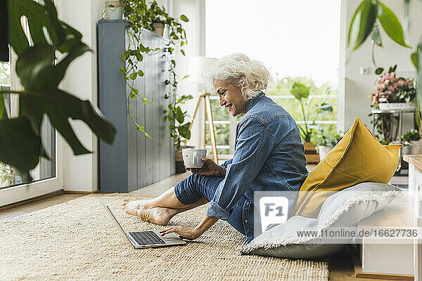 Lächelnde reife Frau arbeitet am Laptop  während sie zu Hause sitzt