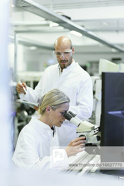 Eine Wissenschaftlerin forscht  während ein männlicher Kollege im Labor in ein Mikroskop schaut