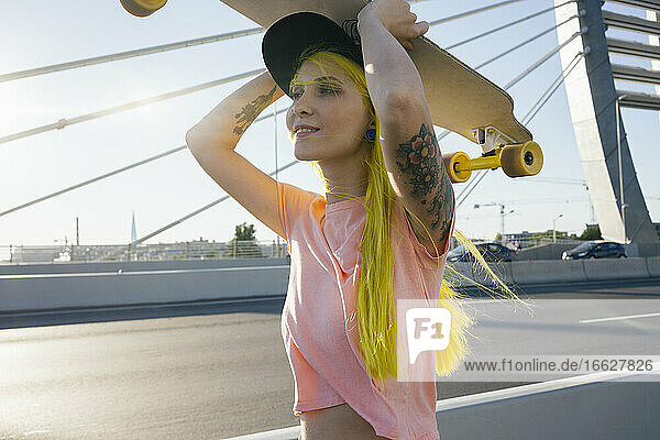 Junge Frau mit Skateboard auf dem Kopf an einem sonnigen Tag