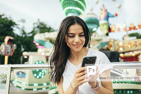 Lächelnde schöne Frau mit Smartphone im Vergnügungspark