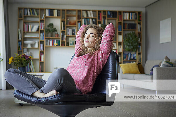 Mittlere erwachsene Frau mit Händen hinter dem Kopf entspannt auf einem Stuhl zu Hause