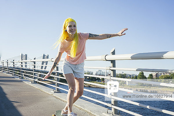 Hipster female doing skating on bridge during sunny day