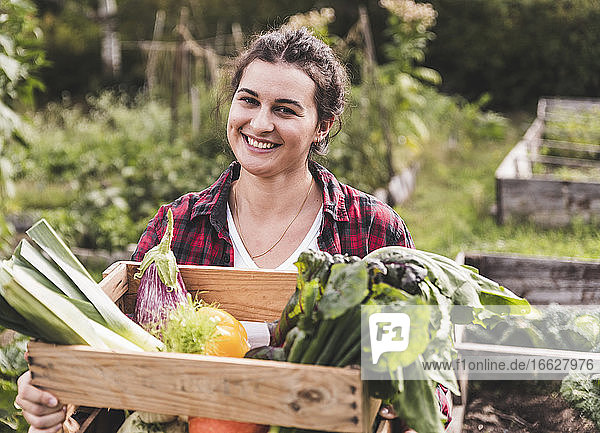 Close-up of smiling woman with vegetables in crate sitting at garden