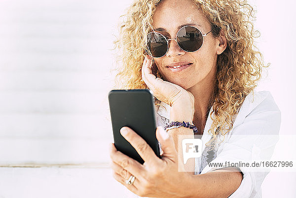 Nahaufnahme einer Frau mit Sonnenbrille  die ein Smartphone benutzt  während sie im Freien sitzt