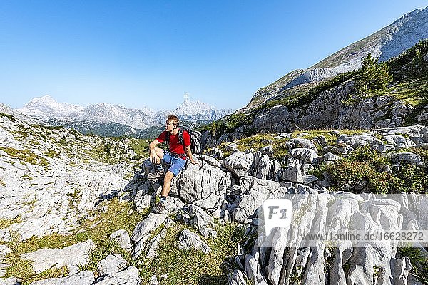 Wanderer sitzt auf einem Stein  hinten Gipfel des Watzmann  Wanderweg in den Funtenseetauern  Steinernes Meer  Nationalpark Berchtesgaden  Berchtesgadener Land  Oberbayern  Bayern  Deutschland  Europa