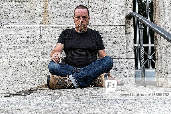 Berlin  Deutschland  Porträt eines erwachsenen  kaukasischen Mannes  der vor einer grauen Wand sitzt.