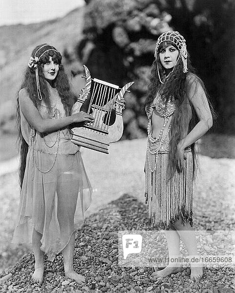 Hollywood  Kalifornien  um 1920.
Zwei Schauspielerinnen in exotischer Kleidung posieren mit einer perlenbesetzten Harfe in einer Szene aus einem frühen Stummfilm.
