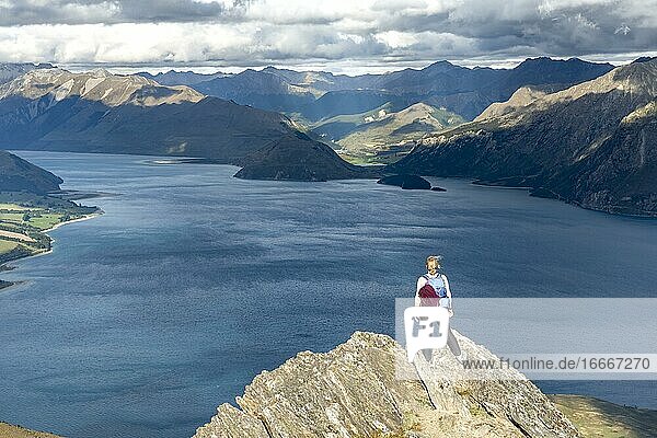 Hiker stands on a rock  view over Lake Hawea  lake and mountain landscape in the evening light  view from Isthmus Peak  Wanaka  Otago  South Island  New Zealand  Oceania