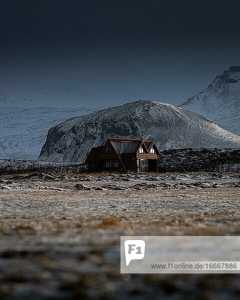 Rotes Haus vor beschneitem Berg mit dramatischer Lichtstimmung  Olafsvik  Island  Europa