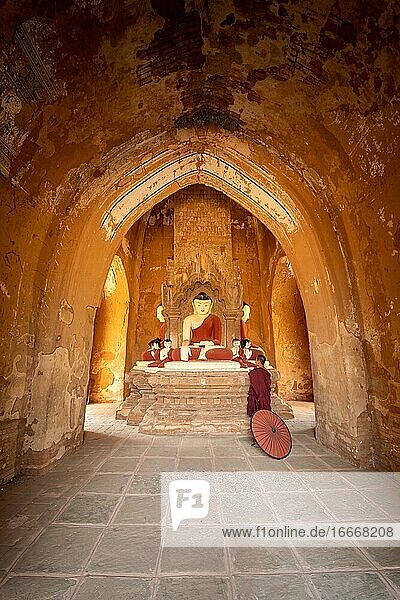 Buddhist young monk in red robe with red umbrella standing in a temple and praying Bagan Myanmar Asia