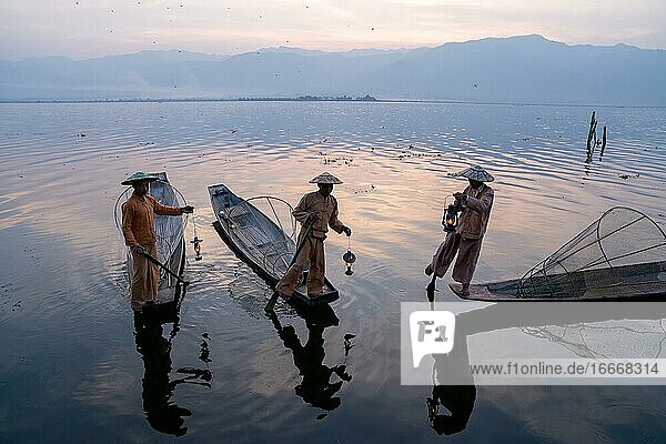 Drei traditionelle Fischer stehen mit Lampen auf ihren kleinen Booten  bei Sonnenaufgang  Lake Inle  Myanmar  Asien
