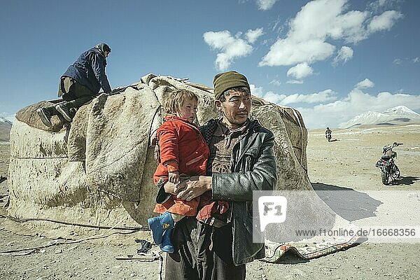 Mann trägt Kind auf dem Arm  nomadische Kirgisen  dahinter traditionelle Jurte  die gerade abgebaut wird  Hochebene von Bozai Gumbaz  Wakhan-Korridor  Badachschan  Afghanistan  Asien