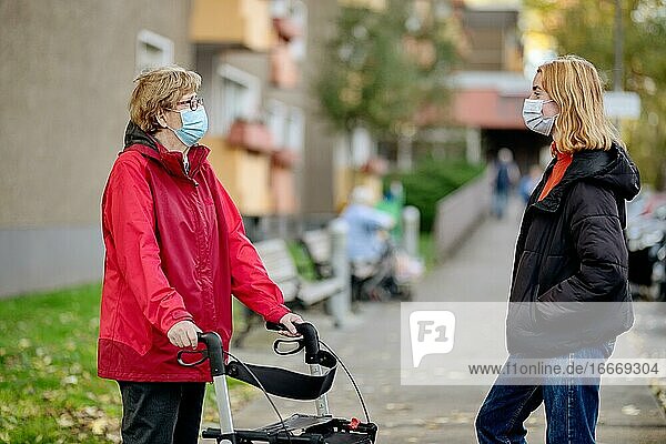 Seniorin mit Rollator und Enkelin vor einem Seniorenwohnheim tragen Mundschutz gegen Corona Viren  Köln  Nordrhein-Westfalen  Deutschland  Europa