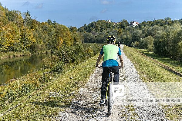Cycle cyclist on cycle path on the canal dam of the Isar  in the back Grünwalder Burg  Grünwald  Upper Bavaria  Bavaria  Germany  Europe