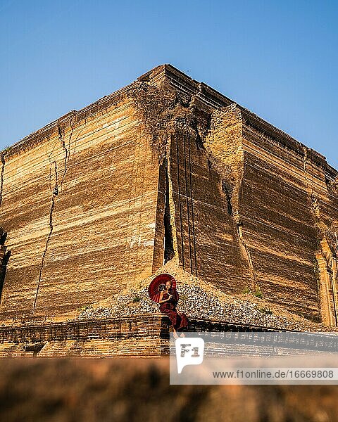 Buddhist monk sitting with red umbrella in front of Mingun Pagoda Mingun Myanmar Asia