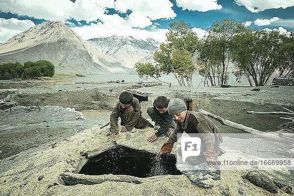 Three boys shovel wheat grains through the opening from above into a granary members of the ethnic group of the sedentary Wakhi Saradh-e-Broghil Wakhan Corridor Afghanistan Asia