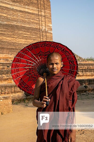 Buddhist monk stands with red umbrella in front of Mingun Pagoda Mingun Myanmar Asia
