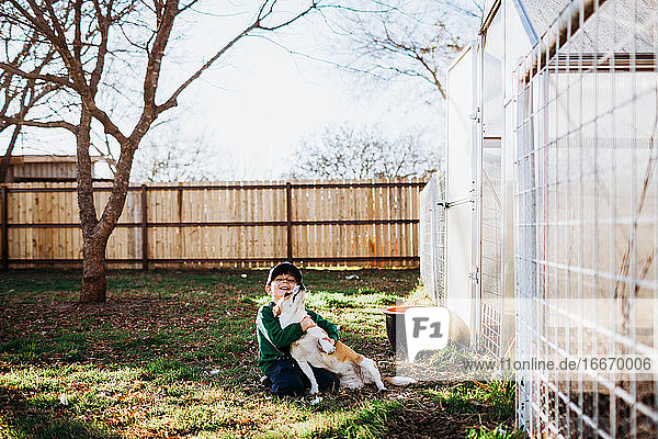 Junger Junge sitzt vor einem Gartenhaus und umarmt einen Corgi-Hund