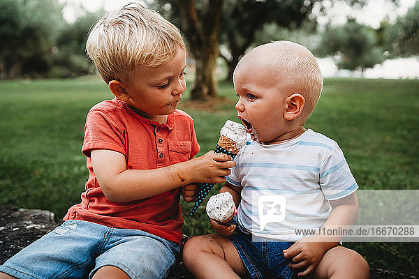 Junges weißes Kleinkind gibt Bruder Eis in einem heißen Sommertag