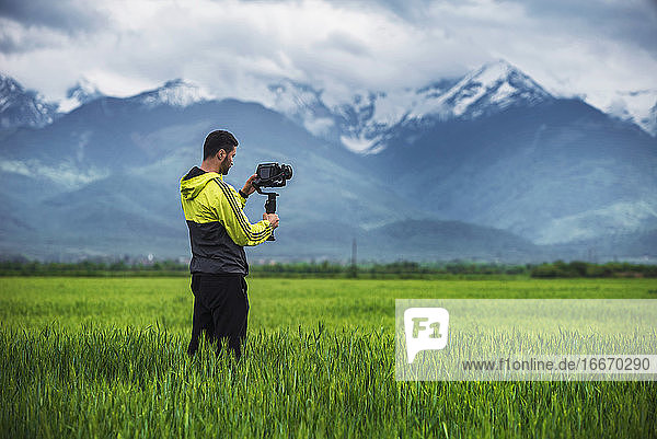 Man holding camera on a stabilizer on a green field  scenic background