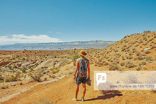 Rücken eines jungen Mannes mit Hut  der während einer Wanderung in die Wüste blickt.