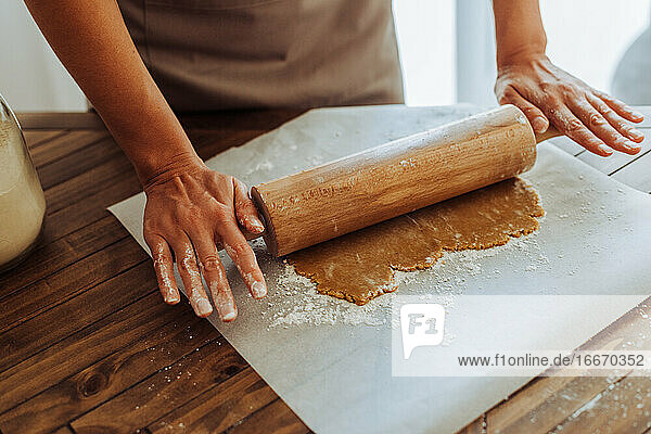 Nahaufnahme von Händen  die Teig für Kekse am Tisch ausrollen