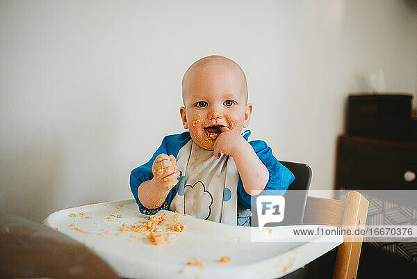 Entzückendes Baby lernt zu essen und macht ein Durcheinander Finger im Mund