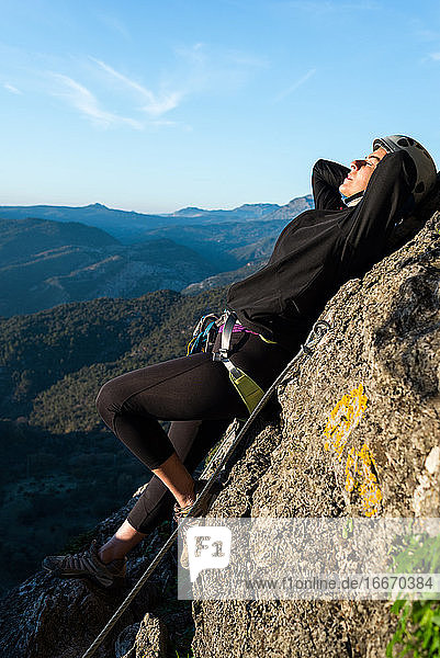 Konzept: Abenteuer. Bergsteigerin mit Helm und Klettergurt. Liegt auf einem Felsen und nimmt ein Sonnenbad. Via ferrata in den Bergen.