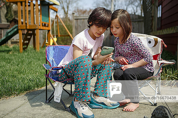 Zwei Kinder sitzen mit den Köpfen zusammen und schauen auf ein mobiles Gerät